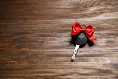 Photo of Key with red bow and space for text on wooden background, top view. Car buying
