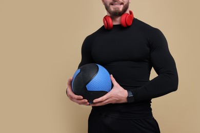 Photo of Sportsman with headphones and medicine ball on brown background, closeup. Space for text