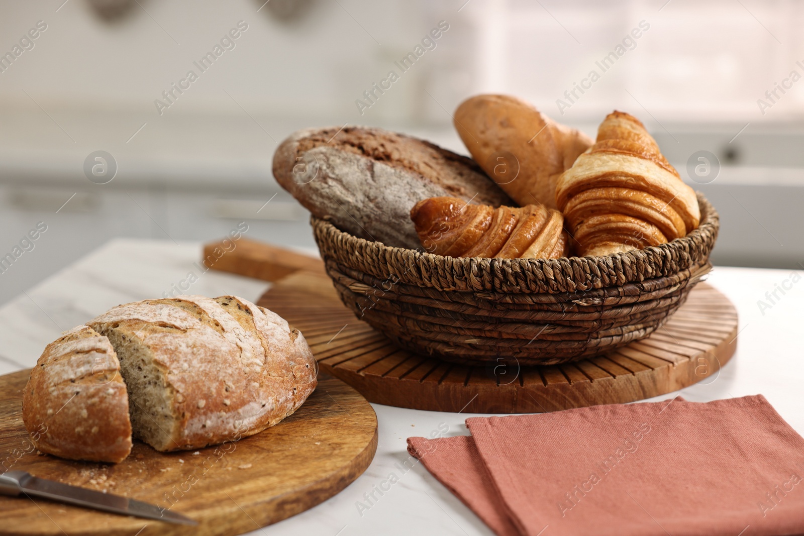 Photo of Wicker bread basket with freshly baked loaves and knife on white marble table in kitchen