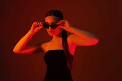 Photo of Portrait of beautiful young woman in sunglasses on color background with neon lights