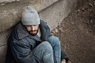 Photo of Poor homeless man sitting near wall on street. Space for text