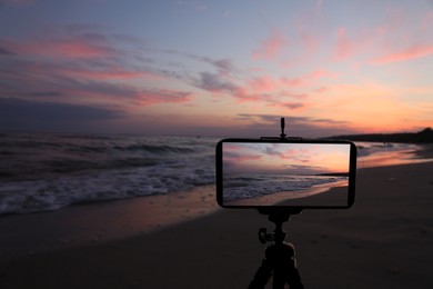 Taking photo of beautiful sandy beach at sunset with smartphone mounted on tripod