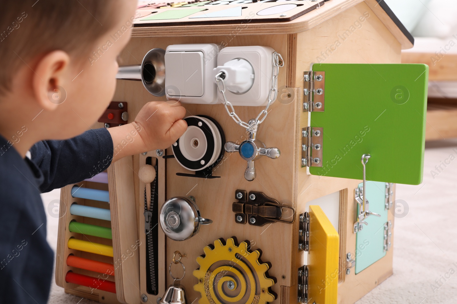 Photo of Little boy playing with busy board house on floor, closeup