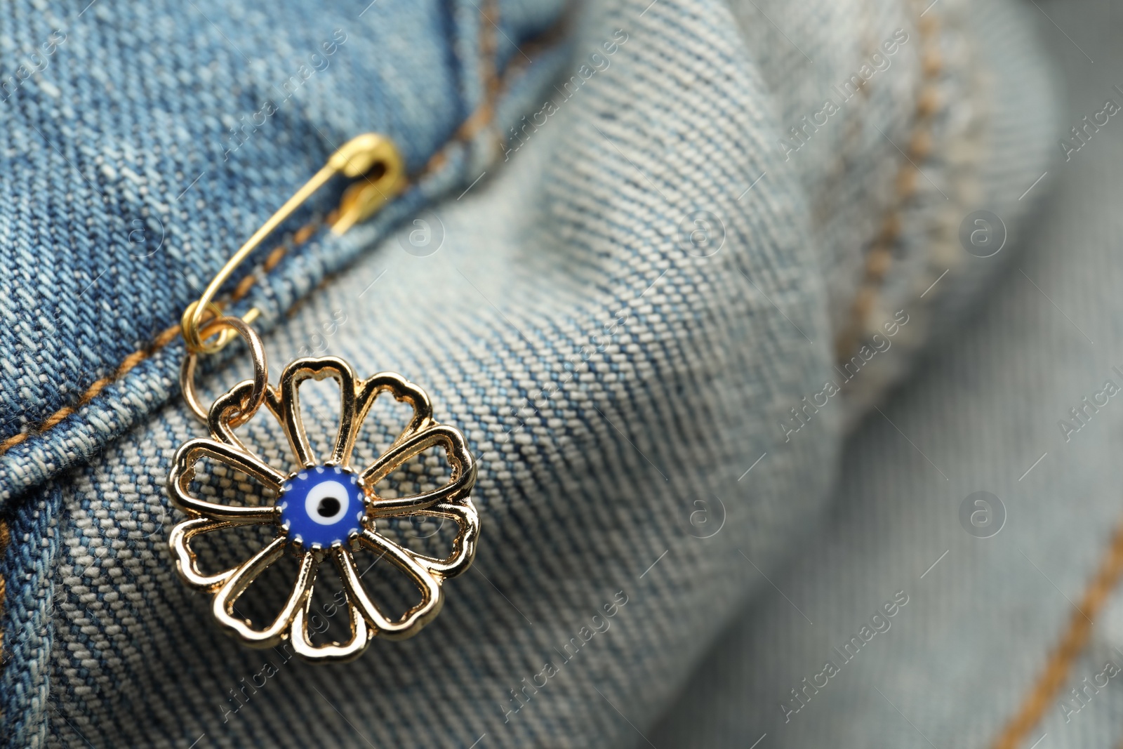 Photo of Evil eye safety pin on denim clothing, closeup