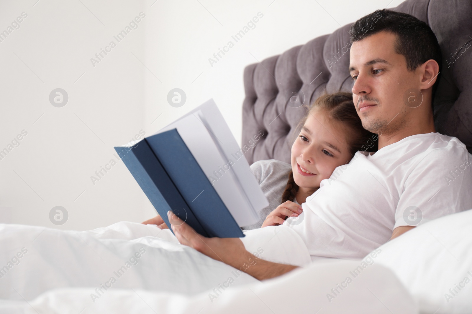 Photo of Father reading book with child in bedroom. Happy family