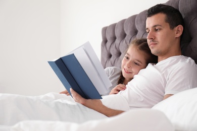 Photo of Father reading book with child in bedroom. Happy family