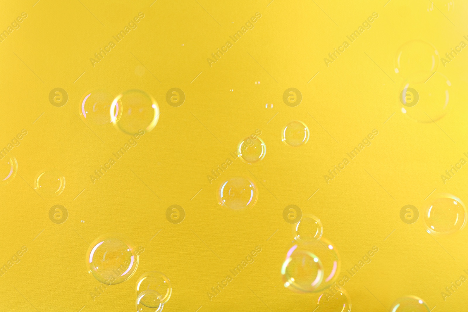 Photo of Beautiful transparent soap bubbles on yellow background