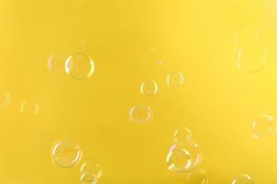 Photo of Beautiful transparent soap bubbles on yellow background