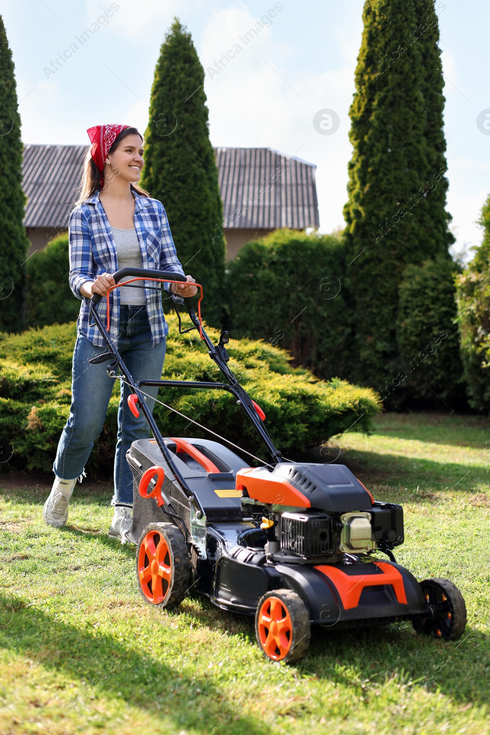 Photo of Smiling woman cutting green grass with lawn mower in garden