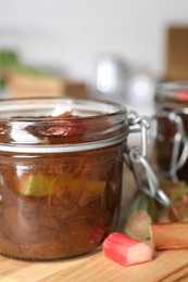 Photo of Jar of tasty rhubarb jam and cut stems on wooden table, closeup