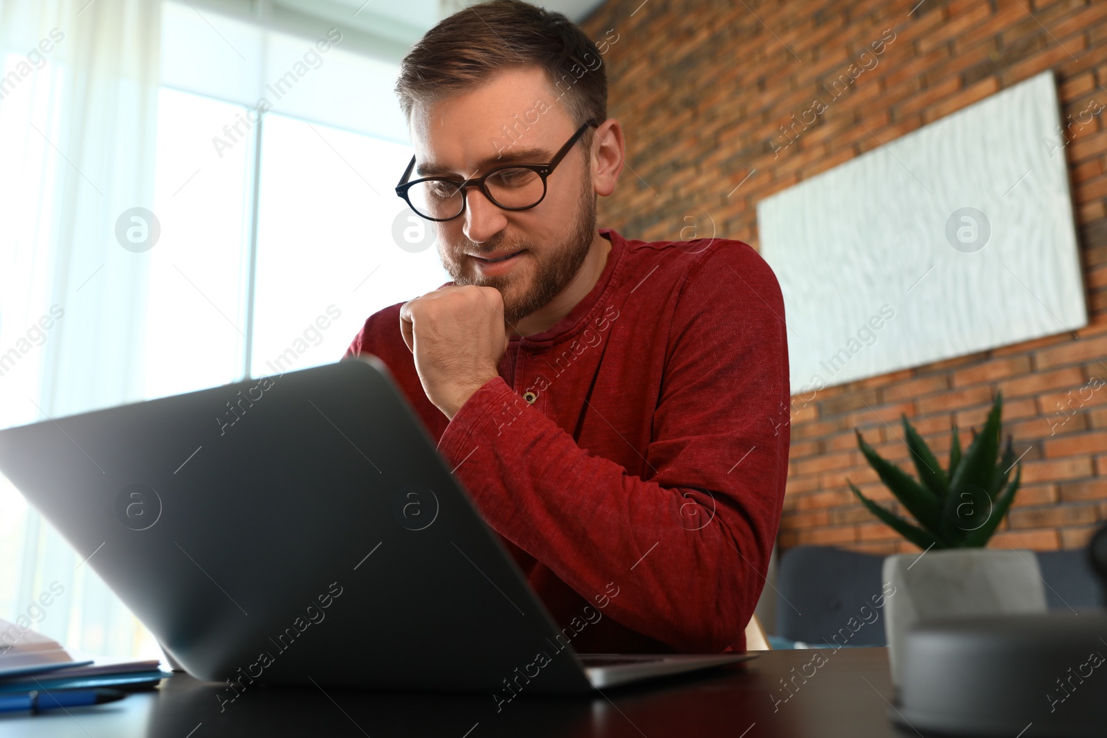 Photo of Young man using laptop at table indoors