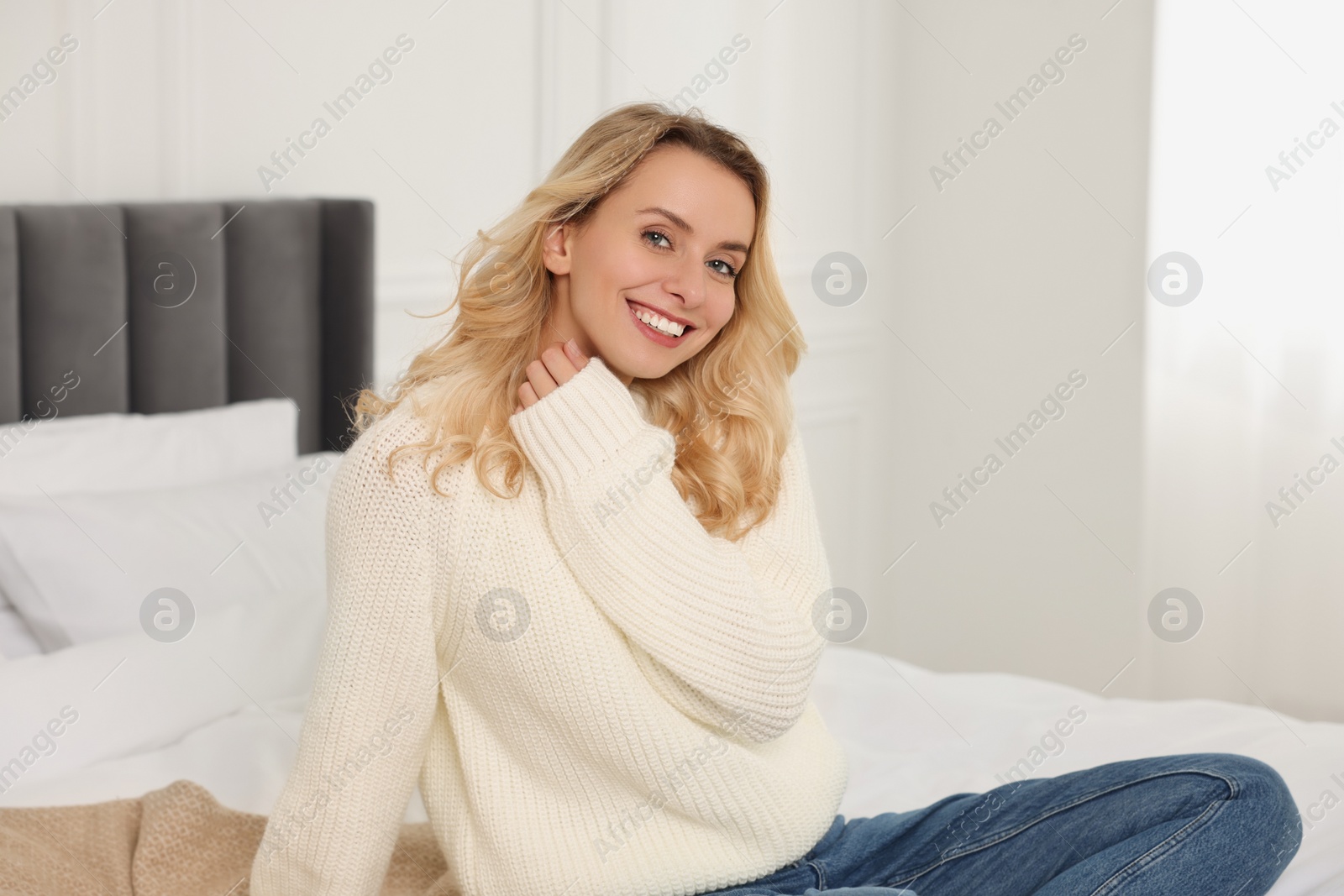 Photo of Happy woman in stylish warm sweater on bed at home