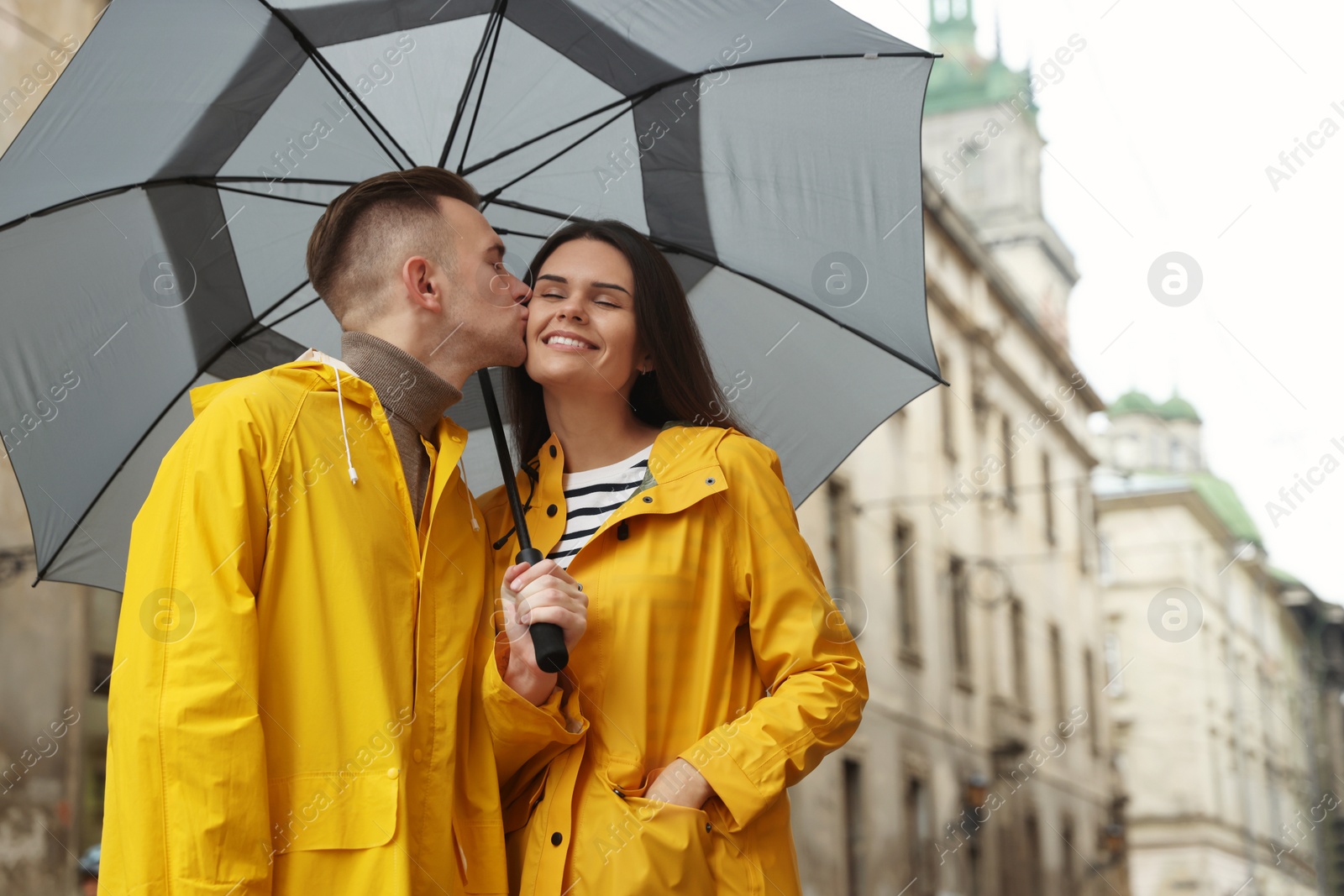 Photo of Lovely young couple with umbrella kissing under rain on city street