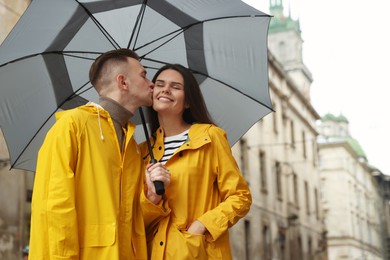 Lovely young couple with umbrella kissing under rain on city street