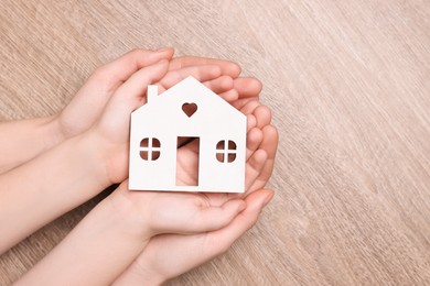 Photo of Home security concept. Woman and her little child holding house model at wooden table, top view with space for text