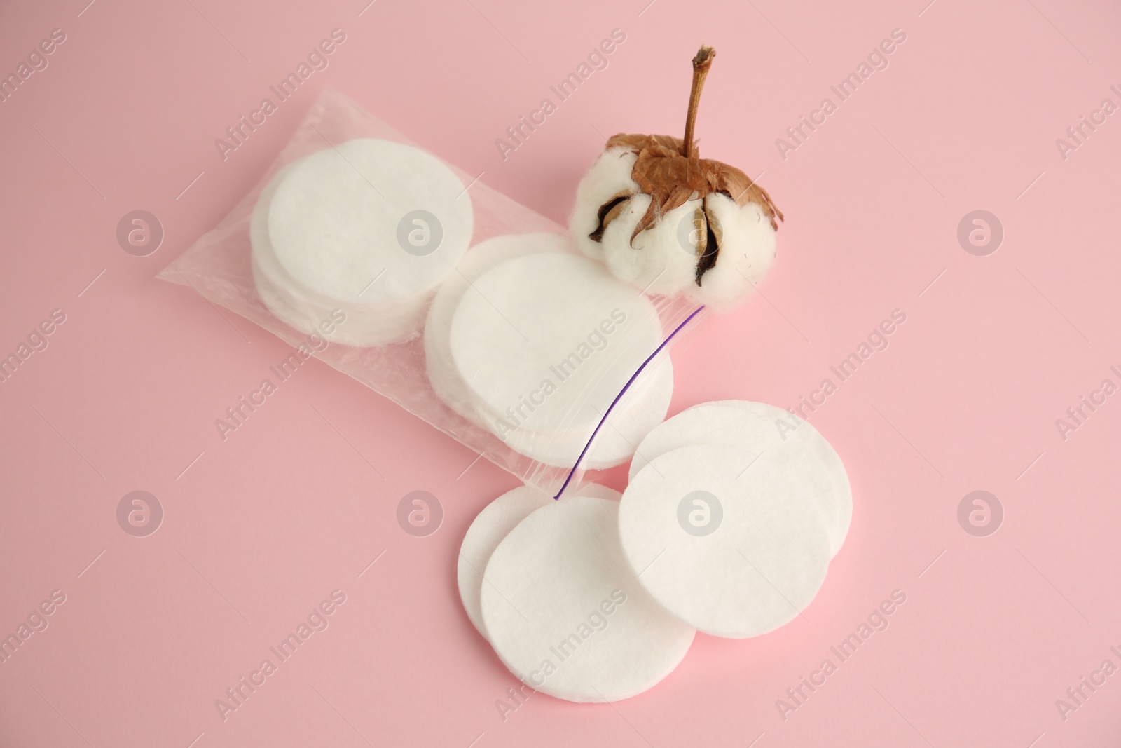 Photo of Plastic bag with cotton pads and flower on pink background