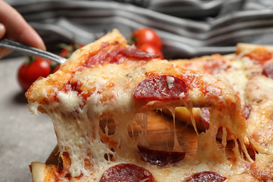 Photo of Woman taking slice of tasty pepperoni pizza at table, closeup