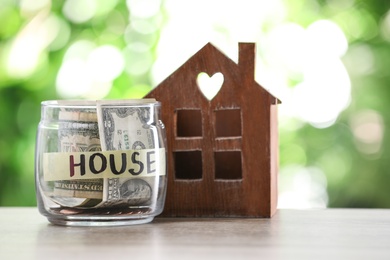 Glass jar with money for mortgage and house model on table against blurred background