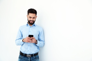 Handsome young man using phone near white wall, space for text. Working time