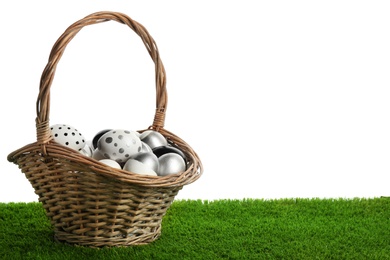Photo of Wicker basket of painted Easter eggs on green lawn against white background. Space for design