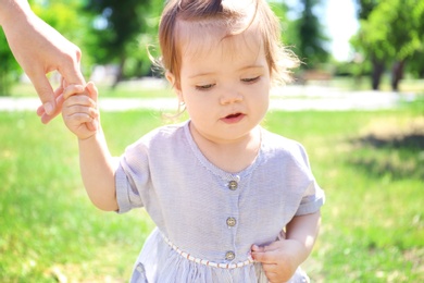 Photo of Adorable baby girl holding mother's hand while learning to walk outdoors