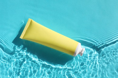 Photo of Tube with moisturizing cream in water on light blue background, top view