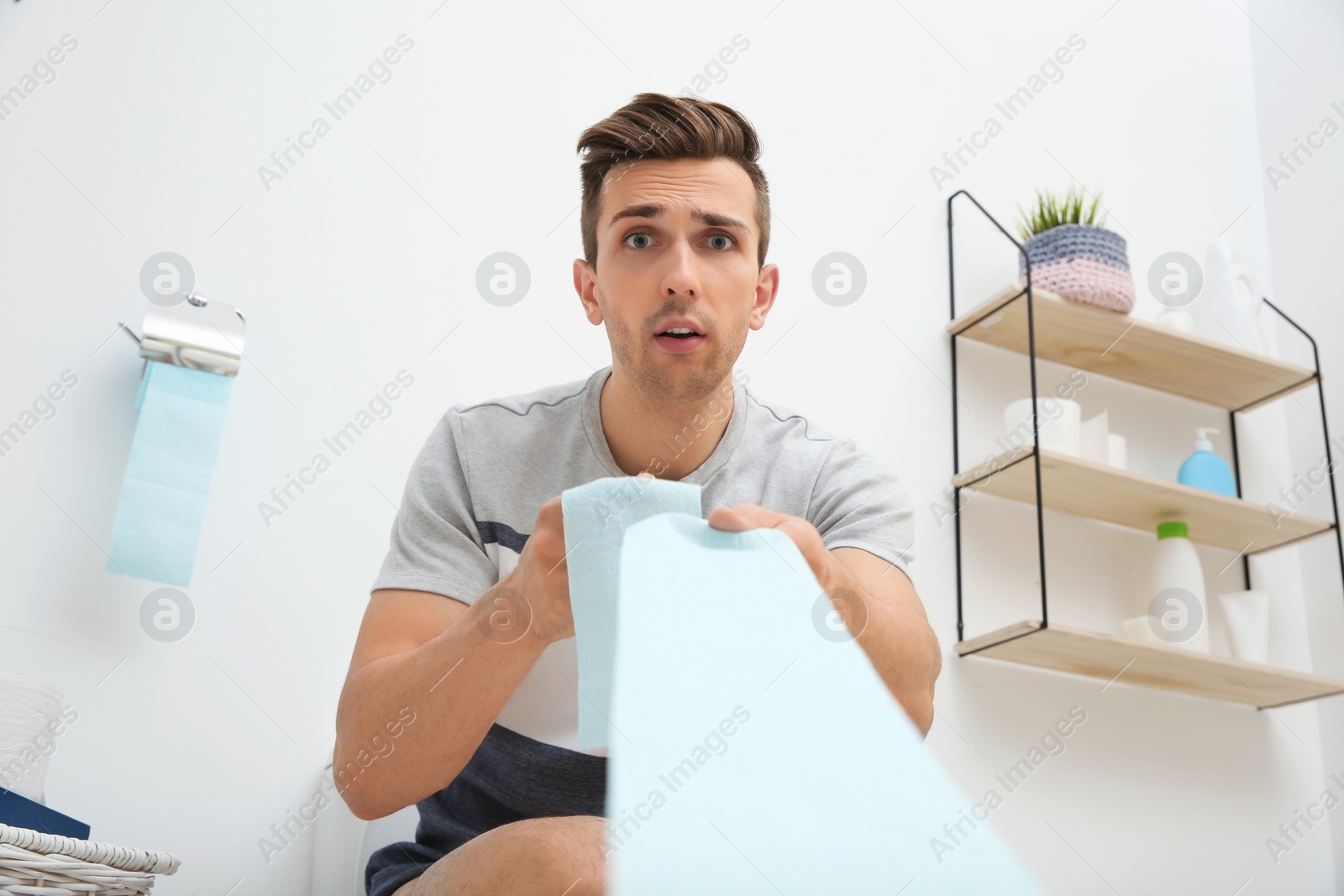 Photo of Young man pulling toilet paper in bathroom