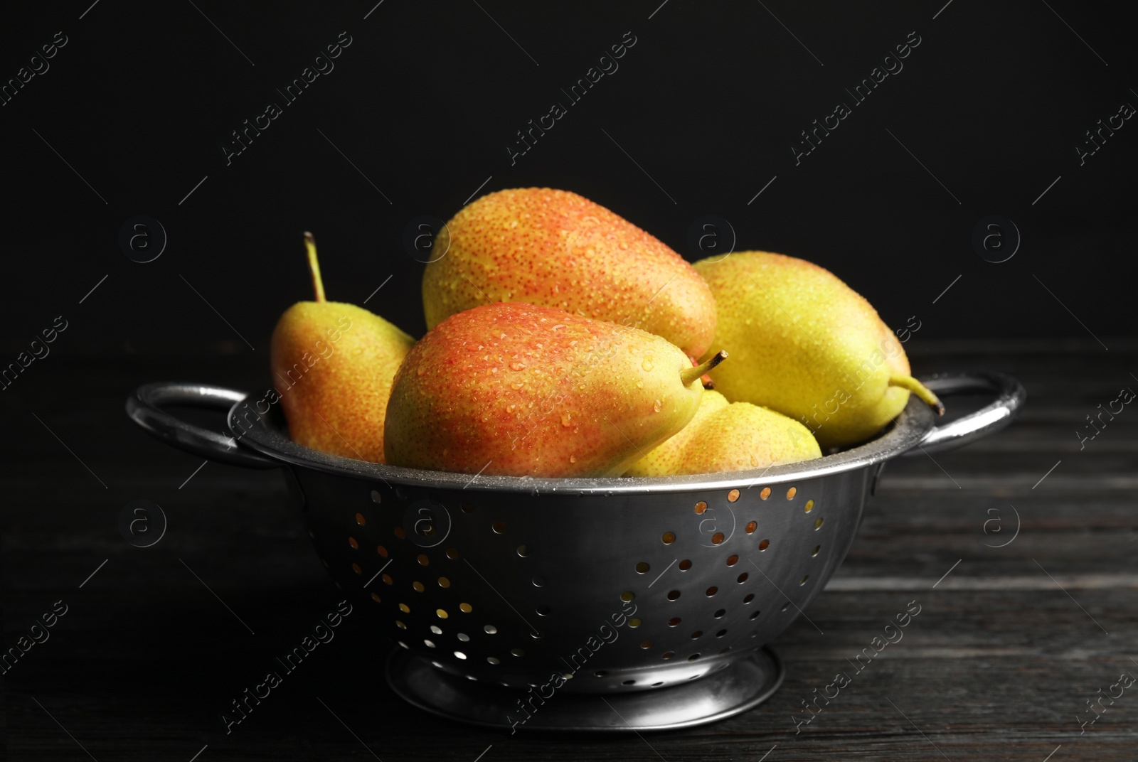 Photo of Colander with pears on dark wooden table against black background