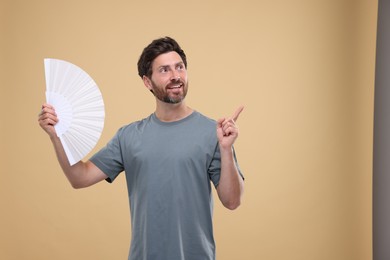 Photo of Happy man holding hand fan on beige background. Space for text