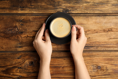 Photo of Woman with cup of coffee at wooden table, top view