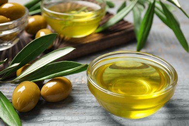 Photo of Bowl of cooking oil, olives and green leaves on wooden table, closeup