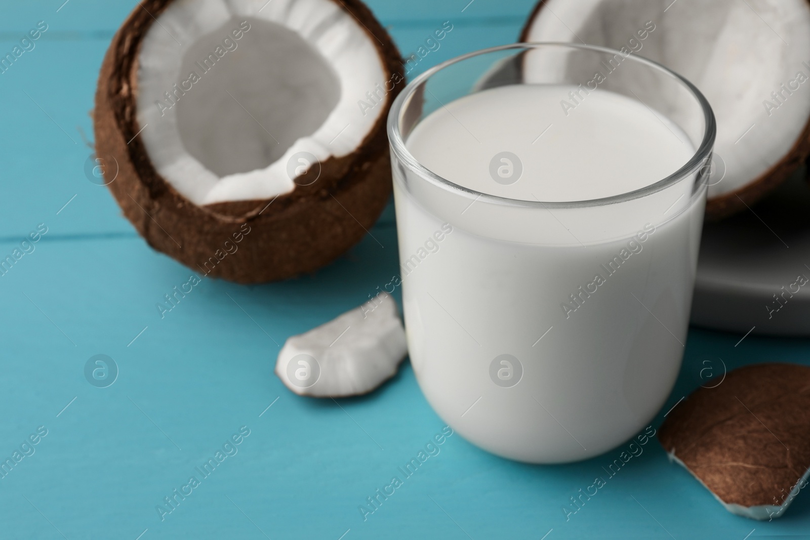 Photo of Glass of delicious vegan milk and coconuts on light blue wooden table