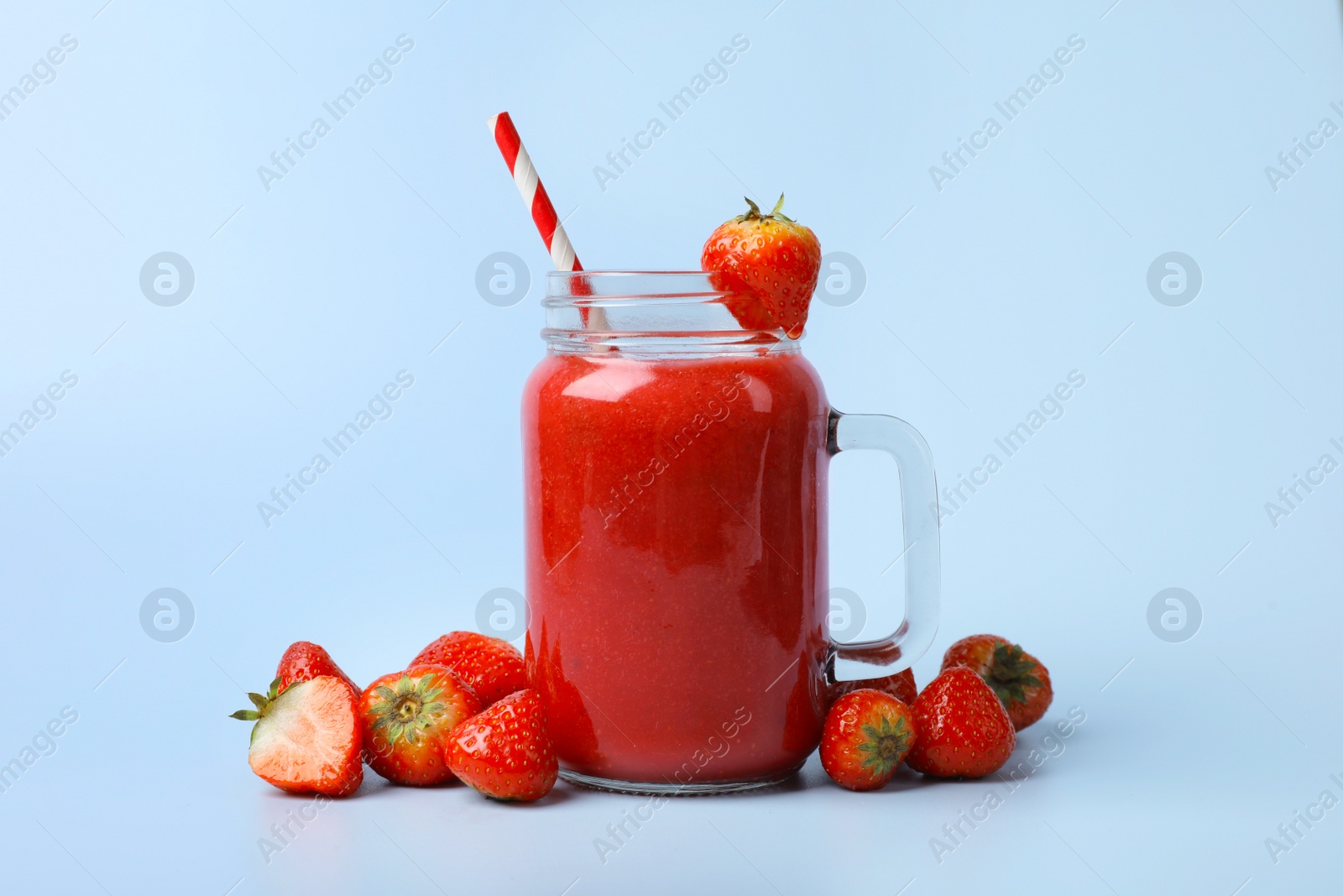 Photo of Mason jar with delicious berry smoothie and fresh strawberries on light blue background