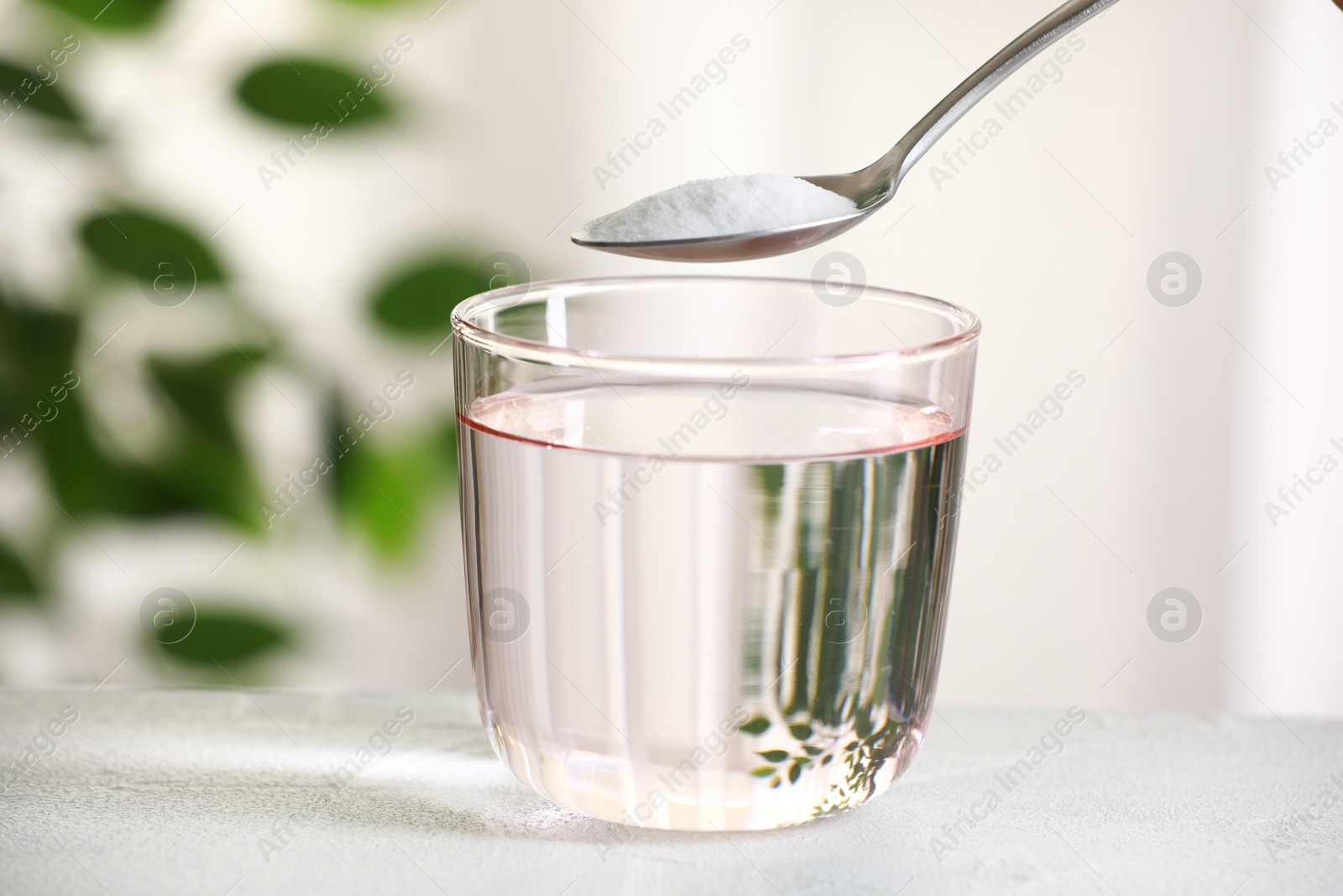 Photo of Spoon with baking soda over glass of water at white table against blurred background, closeup