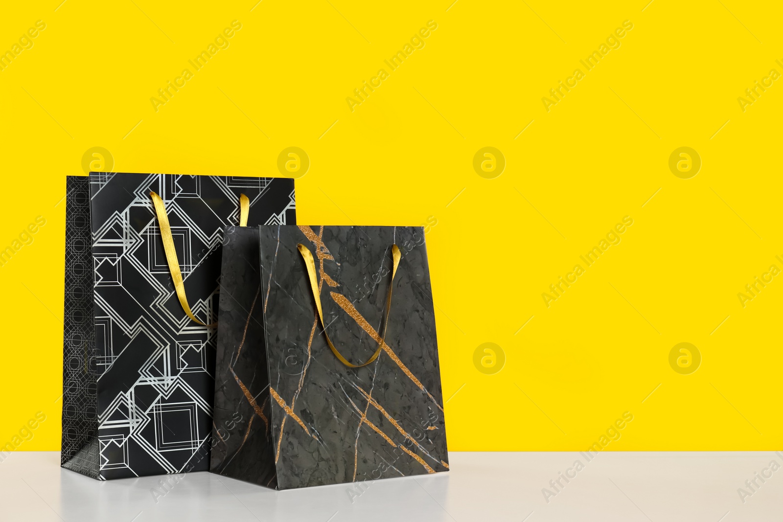 Photo of Stylish shopping paper bags on yellow background. Space for text