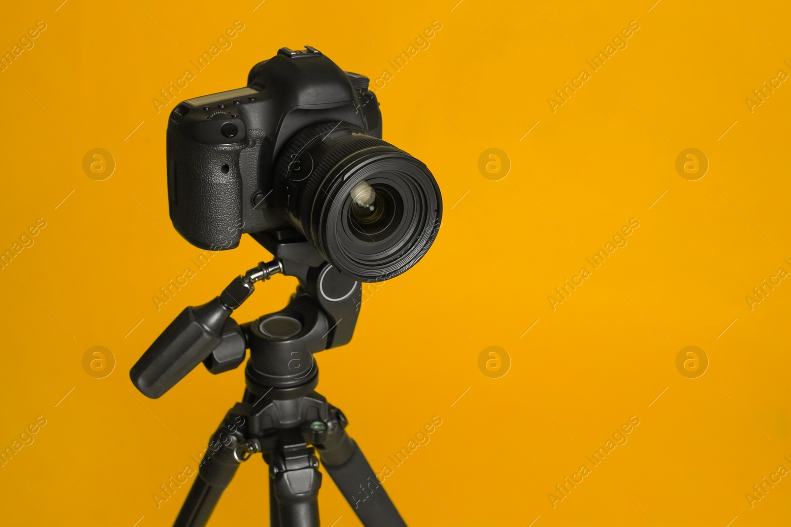 Photo of Modern tripod with professional camera on yellow background. Space for text