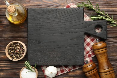 Photo of Black cutting board, napkin and spices on wooden table, flat lay