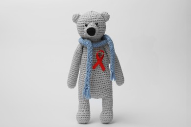 Photo of Cute knitted toy bear with red ribbon on light grey background. AIDS disease awareness