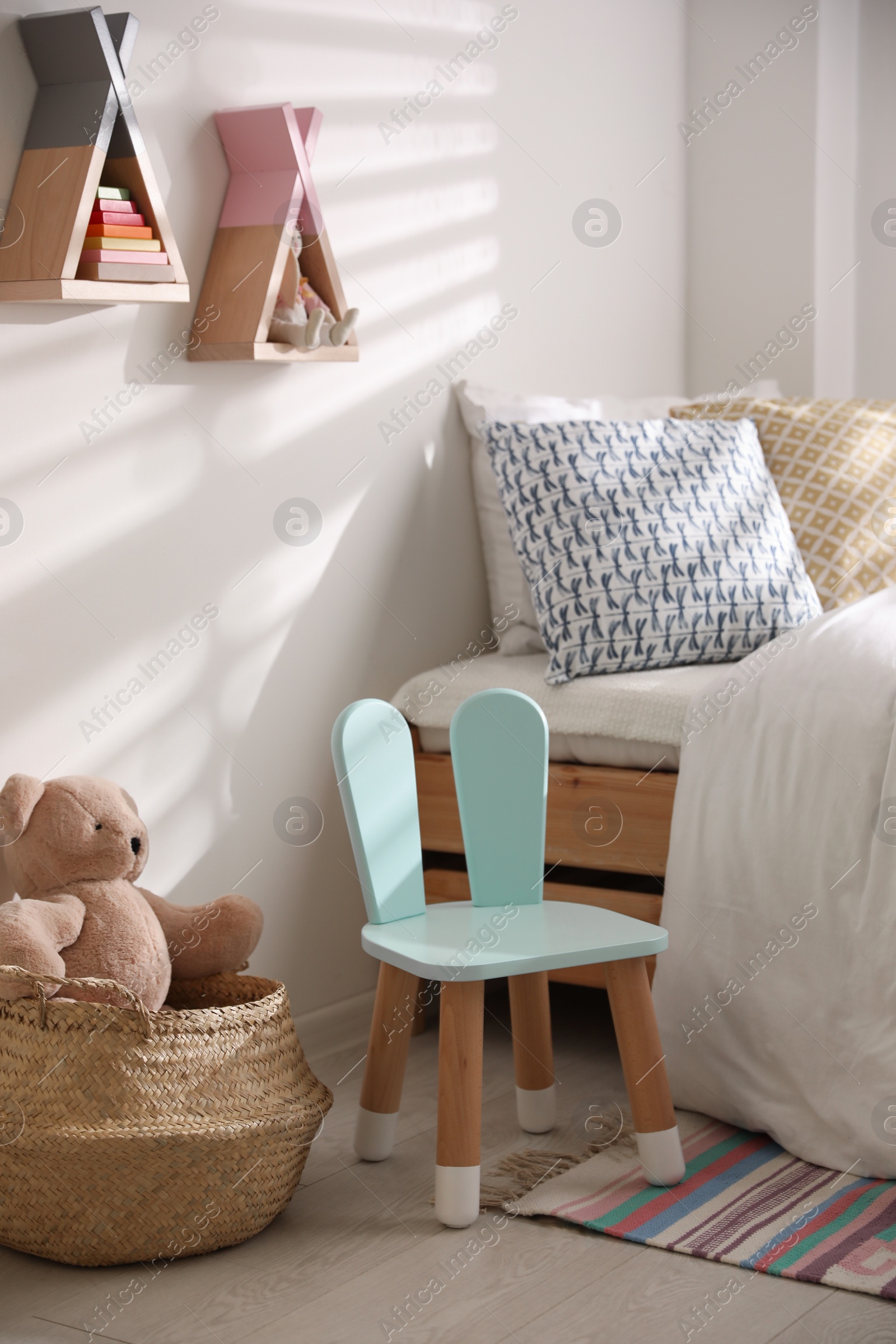 Photo of Cute little chair with bunny ears near bed indoors. Children's room interior