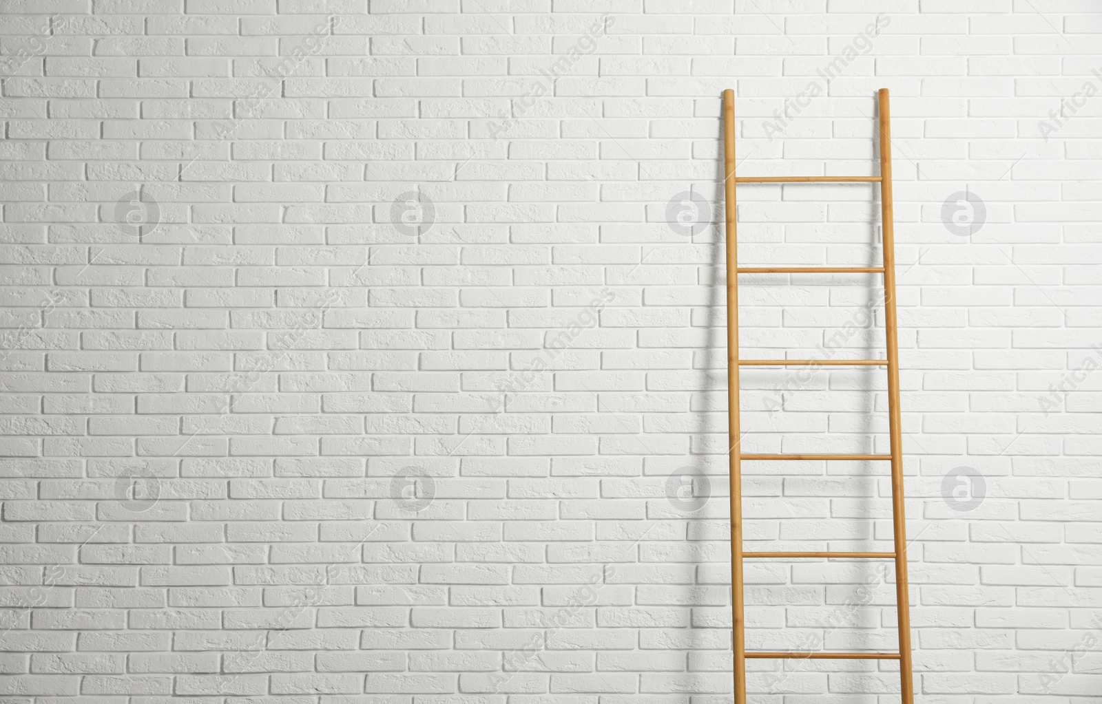 Photo of Modern wooden ladder near white brick wall. Space for text