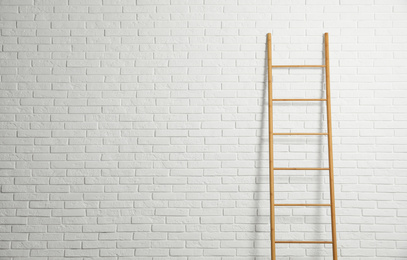 Photo of Modern wooden ladder near white brick wall. Space for text