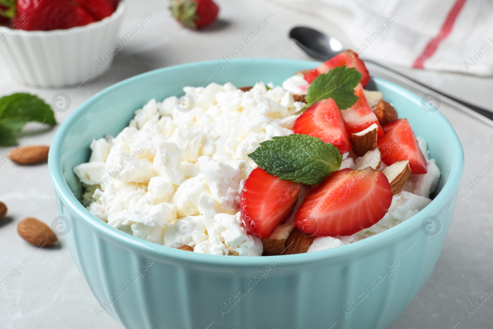 Photo of Fresh cottage cheese with strawberry and almond in bowl on light table, closeup