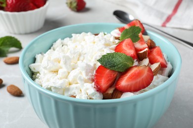 Photo of Fresh cottage cheese with strawberry and almond in bowl on light table, closeup