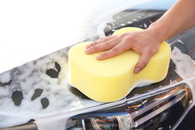 Photo of Worker cleaning automobile with sponge at car wash, closeup