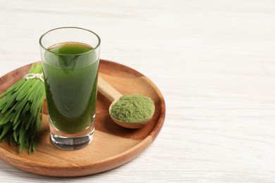 Wheat grass drink in shot glass, spoon of green powder and fresh sprouts on white wooden table, space for text