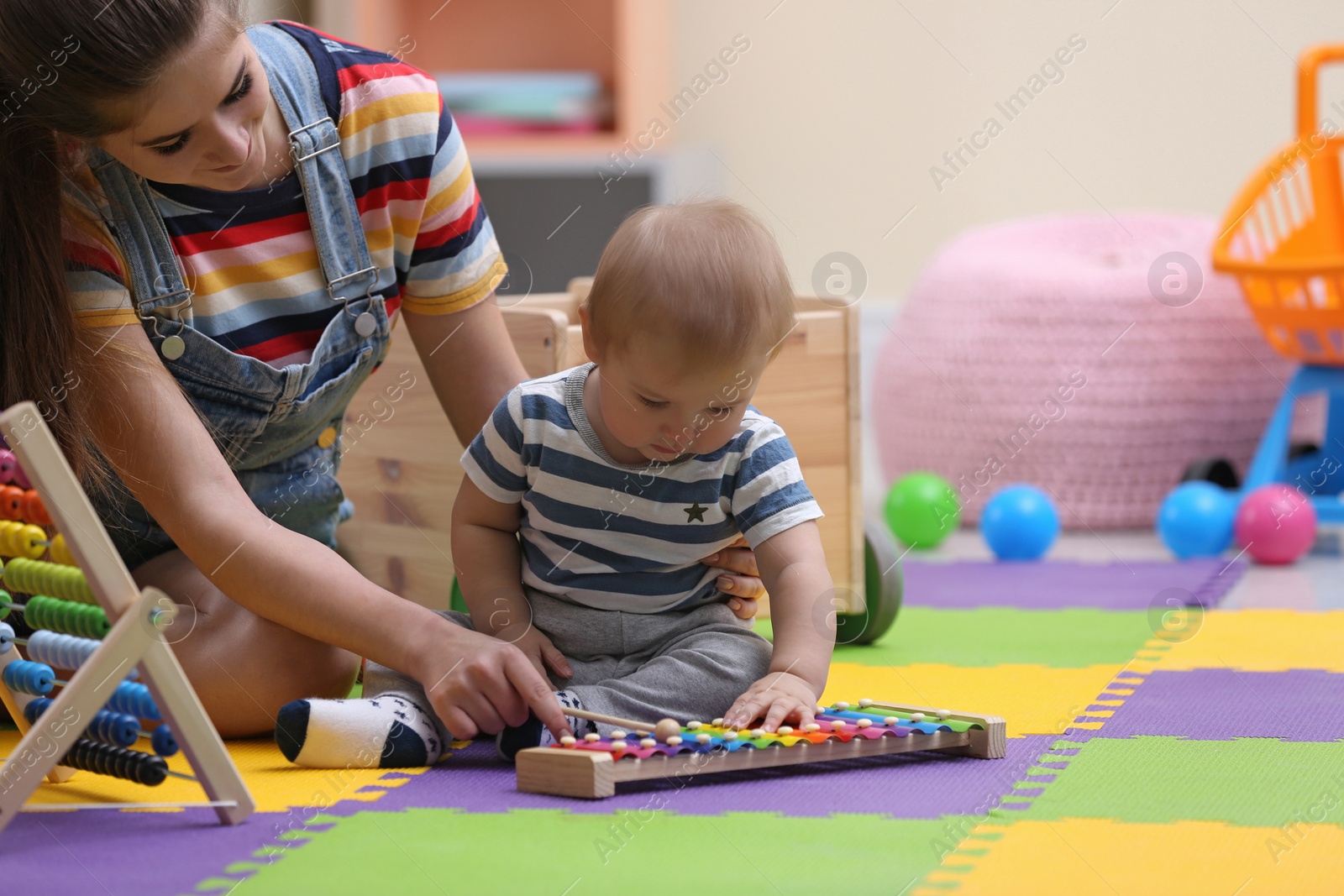 Photo of Teen nanny and cute little baby playing with xylophone at home