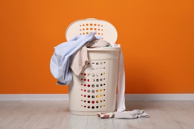 Photo of Laundry basket with clothes near orange wall