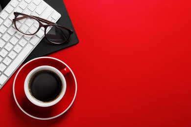Photo of Cup with aromatic coffee, glasses and keyboard on red background, flat lay. Space for text