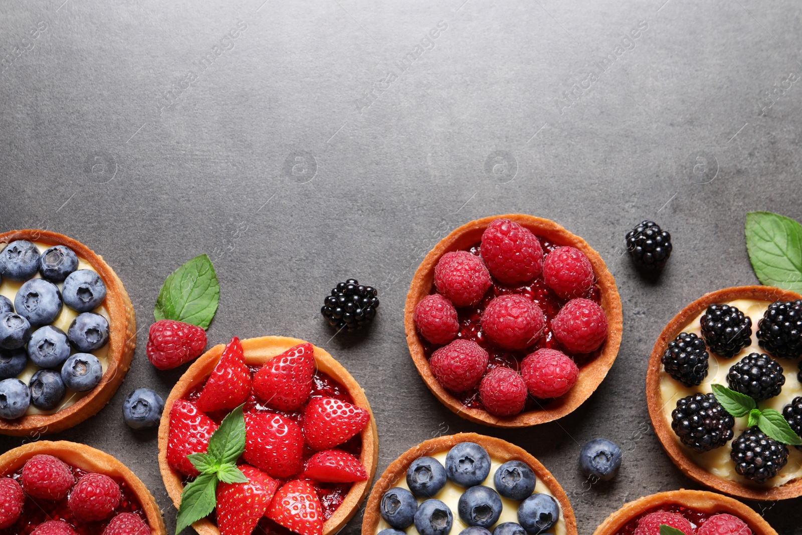 Photo of Tartlets with different fresh berries on grey table, flat lay and space for text. Delicious dessert