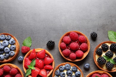 Tartlets with different fresh berries on grey table, flat lay and space for text. Delicious dessert